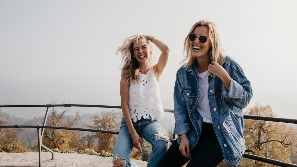 Zwei junge Frauen auf einem Geländer im Schwarzwald. Sie lachen und blicken in die Kamera und sehen so aus, als hätten sie ihre Finanzen im Griff ;)