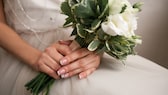 Braut mit French Manicure mit weißen Ornamenten, im Brautkleid und einem Blumenstrauß in der Hand