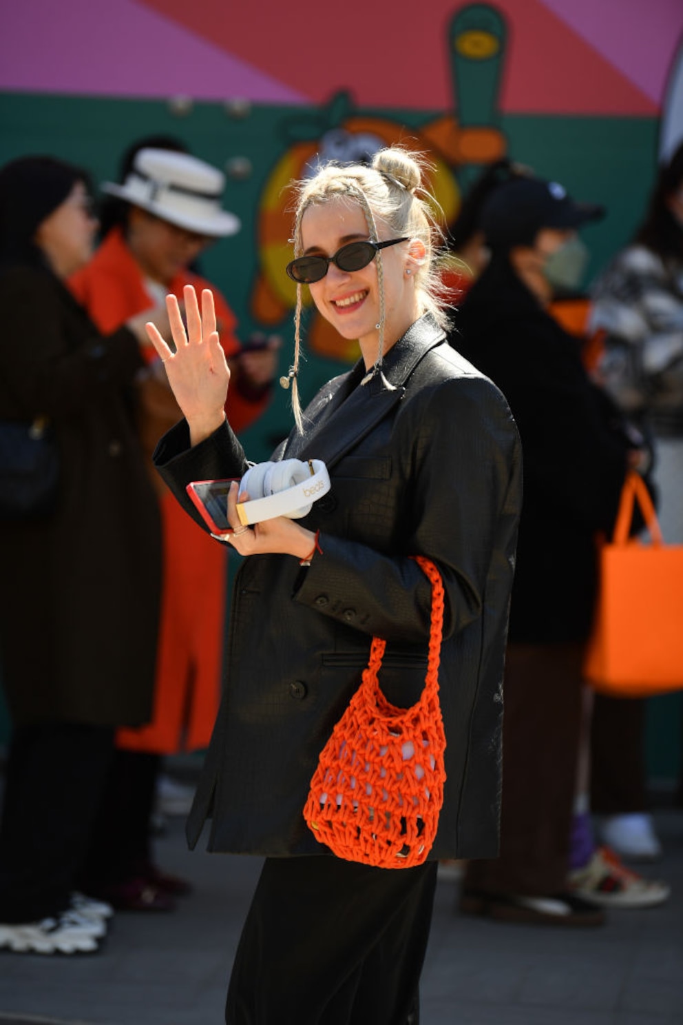 Outfit in Schwarz mit passender Sonnenbrille und einen orangen Häkel-Beutel am Arm besucht diese junge Blondine die Fashion Week in China. 