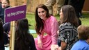 Prinzessin Kate im pinken Kleid. Sie sitzt auf dem Boden neben einigen Kindern, denen sie Rede und Antwort steht und grinst