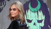 Cara Delevigne lächelt über ihre Schulter in die Kamera. Ihr Make-up ist intensiv und sehr schön, ihre Augenbrauen kommen gut zur Geltung.