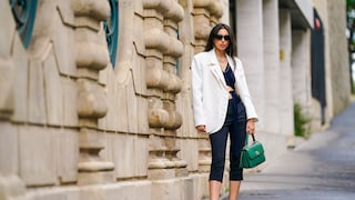 Frau in den Straßen von Paris in dunklen, engen Caprihosen mit schwarzem Top, weißem Blazer und grüner Handtasche