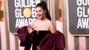 Selena Gomez im schwarzen Off-Shoulder-Kleid mit auberginefarbener Scherpe wie sie lachend in die Kamera winkt