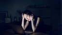 Frau am Laptop mit Kopf in die Hände gestützt im dunklen Büro