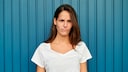 Junge Frau im weißen T-Shirt vor blauer Wand mit grantigem Gesicht