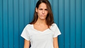 Junge Frau im weißen T-Shirt vor blauer Wand mit grantigem Gesicht