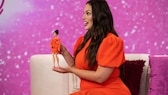 Ashley Graham im orangefarbenen Kleid mit ihrer Barbie-Puppe im selben Kleid