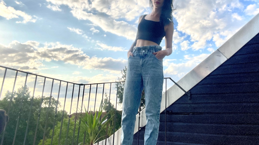 Carmen in Paggy-Jeans, Crop-Top und Pumps auf ihrem Balkon mit Opas selbstgezogener Palme