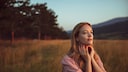 Junge Frau, die in einem Feld vor einem Wald steht und in die schätzungsweise untergehende Sonne blickt. Ein wundervolles Mood-Bild für den Make-up-Trend, wie ich finde. Ich liebe Moods!