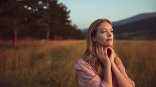 Junge Frau, die in einem Feld vor einem Wald steht und in die schätzungsweise untergehende Sonne blickt. Ein wundervolles Mood-Bild für den Make-up-Trend, wie ich finde. Ich liebe Moods!