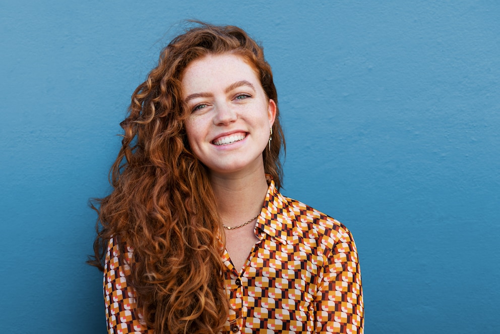 Junge Frau mit roten Locken vor blauer Wand