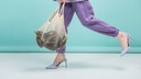 Die Beine einer jungen Dame. Diese stecken in einer dunkelfliederfarbenen Jogginghose. Dazu trägt Sie einen helleren Blazer und farblich passende Pumps und hält einen Beutel mit Auberginen in der Hand, während sie nach links läuft. Das alles vor einem türkisen Hintergrund. Farblich wunderschön und ich habe endlich eine Stylingidee für meinen fliederfarbenen Jogginganzug gefunden! Vorausgesetzt, ich bekomme den Kaffeefleck wieder raus..