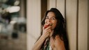 Happy mature woman eating apple by wall