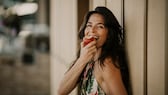 Happy mature woman eating apple by wall