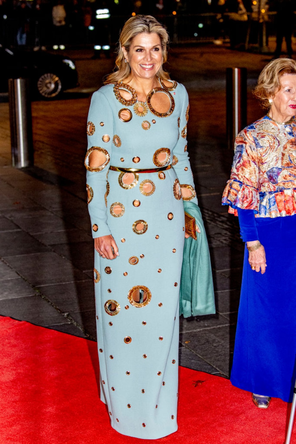 Königin Maxima im hellblauen Kleid mit gold umrandeten Cut-outs auf dem roten Teppich. 