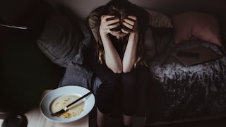Junge Frau, die den Kopf in die Hände stützt. Vor ihr ein leergegessener Teller. Essstörungen sind kein Spaß, bitte holen Sie sich Hilfe.