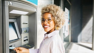 Junge Frau, die lächelnd eine Karte in den Bankautomat steckt