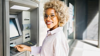 Junge Frau, die lächelnd eine Karte in den Bankautomat steckt