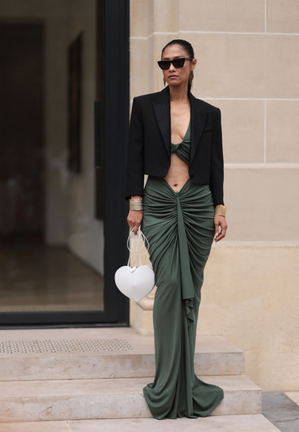 Junge Frau im olivgrünen Kleid mit gerafftem Rock und Cut-out. Ein schwarzer großer Blazer sorgt für den entsprechenden Ausgleich, sodass der Look nicht zu nackt wirkt