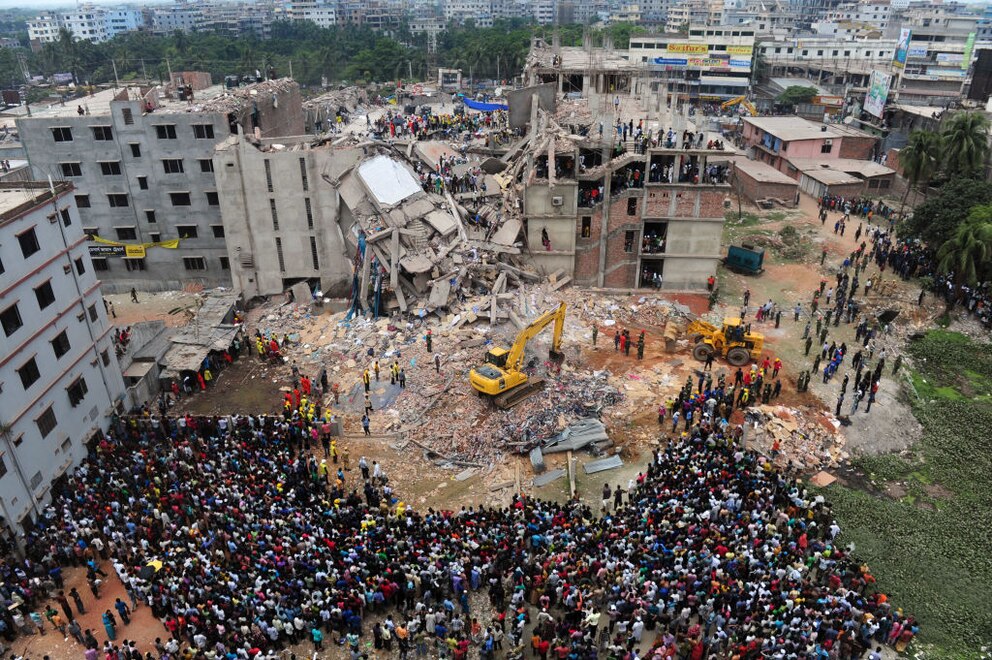 Ein Bild aus der Luft des eingestürzten Rana-Plaza-Gebäudes von 2013. Davor stehen Helfer und Freiwillige.