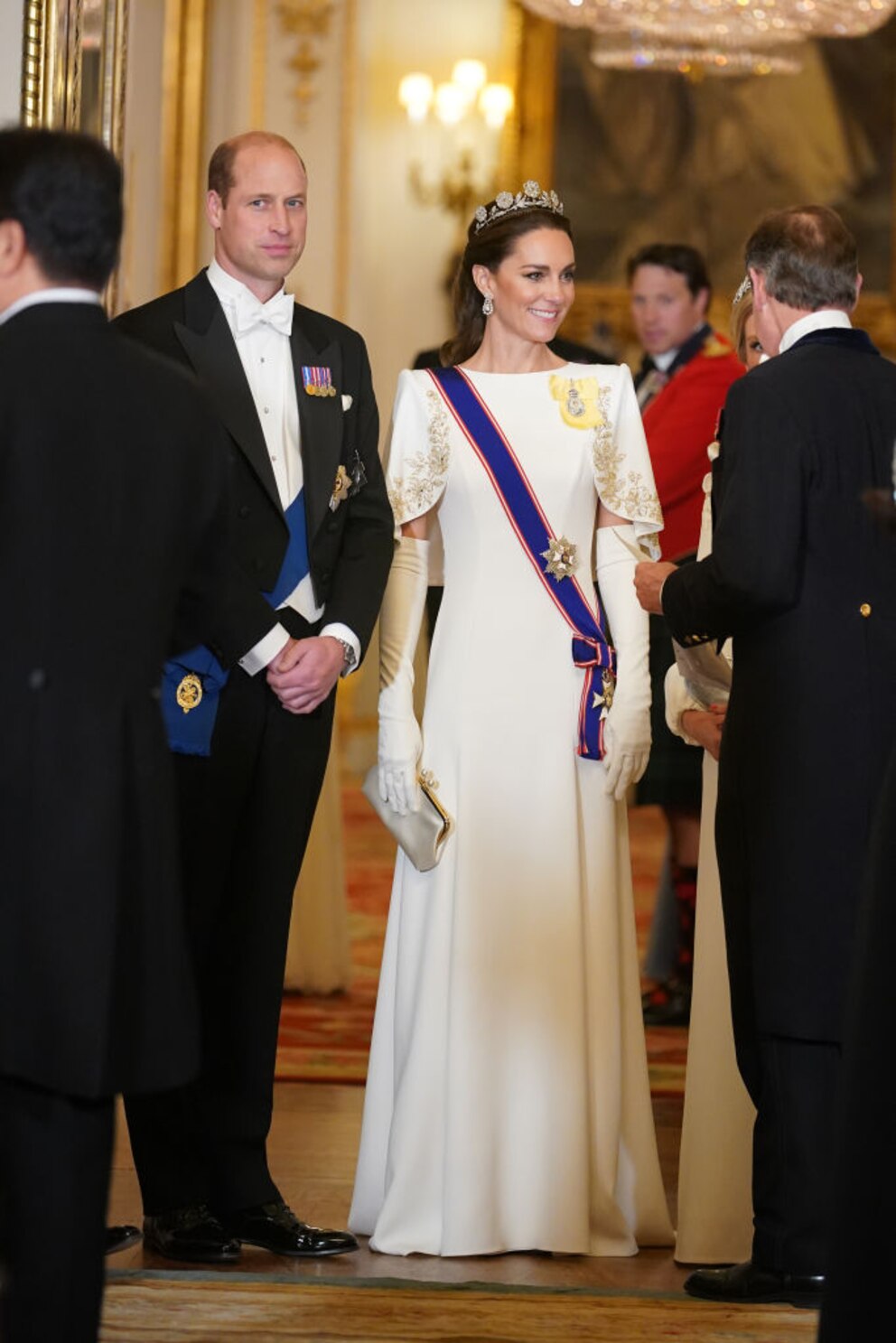 William und Kate. William im Anzug, Kate im weißen Kleid mit Schärpe, Handschuhen und Tiara