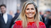 Königin Máxima der Niederlande im roten Outfit, wie sie freudig in die Kamera grinst und dabei sehr symapthisch aussieht