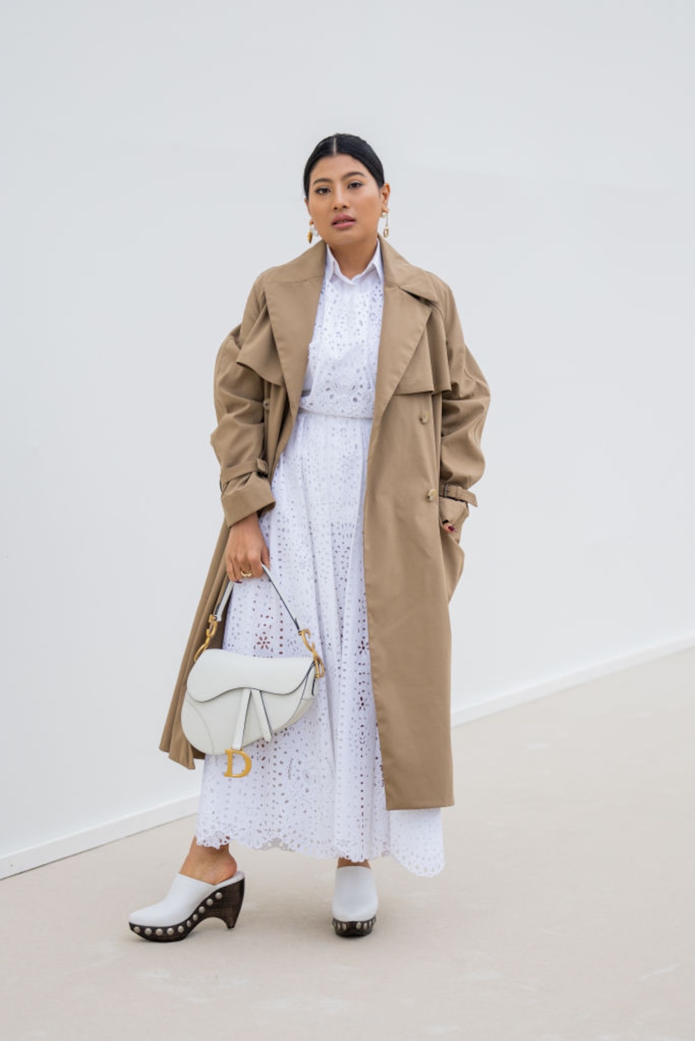 Dame in weißem Kleid, beigem Trenchcoat und weißen Clogs mit Absatz