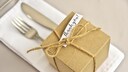 In braunem Karton verpacktes Gastgeschenk auf dem Besteck auf dem Tisch
