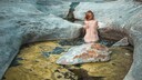 Nackte Frau in Rückenansicht, wie sie auf einem Stein im Wasser sitzt