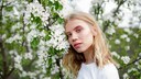 Blonde Frau mit rosa Make-up neben Busch mit weißen Blüten
