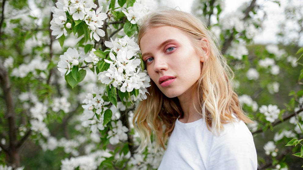 Blonde Frau mit rosa Make-up neben Busch mit weißen Blüten