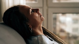 Portrait of a dreadlocks braid woman sitting on the sofa and looking to nowhere. Concept of depression, loneliness, problems of adolescence