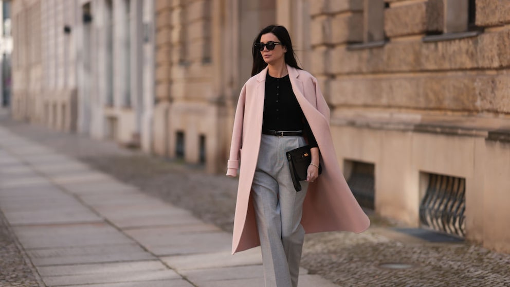 Frau mit Anzughose in Grau, schwarzem Oberteil und Sonnenbrille, dazu rosa Mantel. Streetstyle