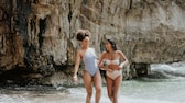 Zwei Frauen in Badeanzug und Bikini im Meer, die sich anlachen und Spaß haben. Ein tolles Shooting, sehr authentisch und schön ohne perfekt zu sein. So wie der Sommer sein sollte