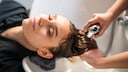 Frau mit Kopf im Waschbecken beim Friseur. Sie hat die Augen geschlossen, lächelt und bekommt die Haare gewaschen