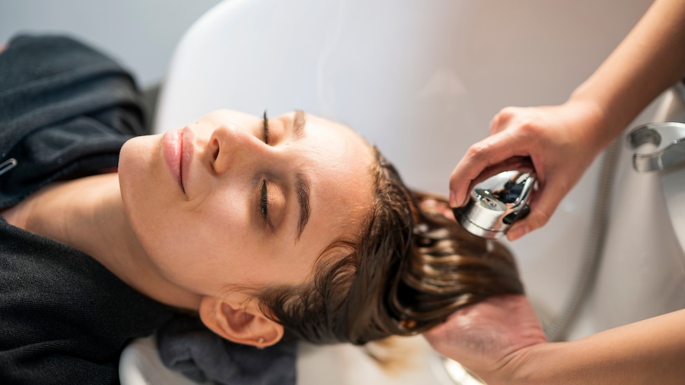 Frau mit Kopf im Waschbecken beim Friseur. Sie hat die Augen geschlossen, lächelt und bekommt die Haare gewaschen