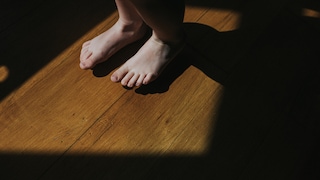 Cute little bare feet stamping on a wooden floor in sunlight.