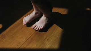 Cute little bare feet stamping on a wooden floor in sunlight.