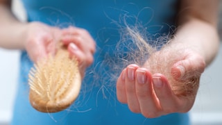 A woman holds a wooden comb in her hands, cleans it of fallen hair after combing. The concept of head health problems, deficient conditions in the body due to stress and depression, a consequence of chemotherapy and radiation for cancer.