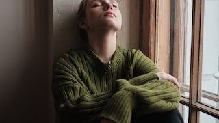 Grief and Depression. Sad depressed girl sitting by window with closed eys, feeling upset, coping with breakup. Unhappy redhead woman at home. People and mental health