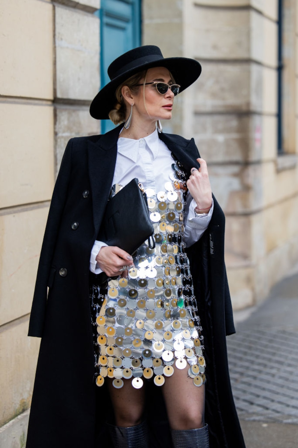 Streetstyle. Silber glitzerndes Kleid, weiße Bluse, schwarze Boots, schwarzer Mantel, Hut, Sonnenbrille und Clutch