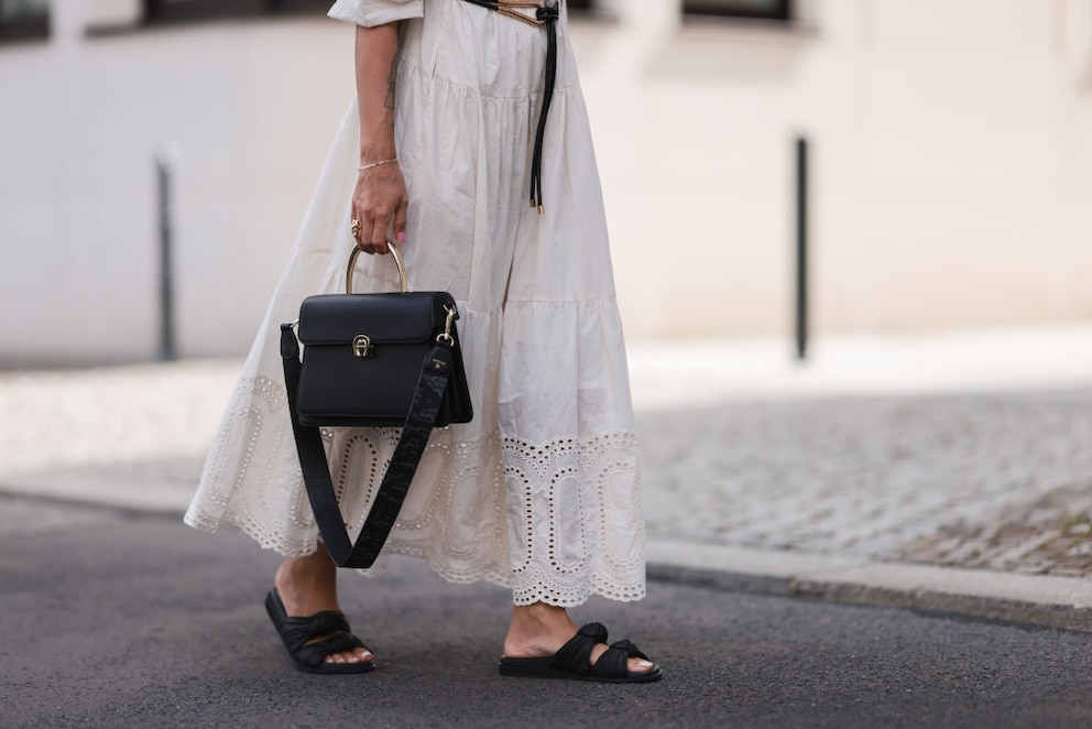 Close-up von weißem, hippiesquem Kleid mit schwarzer Handtasche und Pantoletten