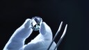 Behandschuhte Hand hält Diamant und Zange vor schwarzem Hintergrund