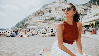 Frau mit rotem Top und weißem Rock und Sonnenbrille am Strand in Positano