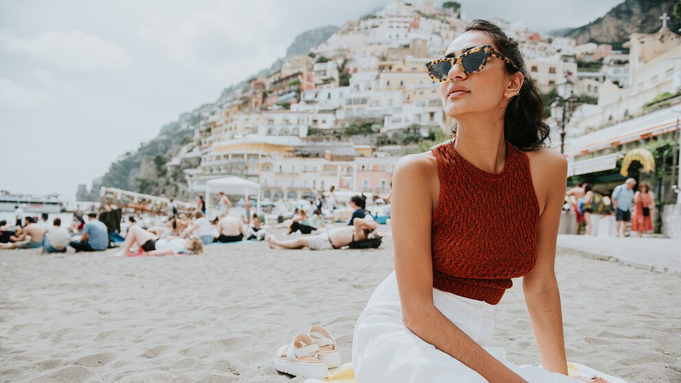 Frau mit rotem Top und weißem Rock und Sonnenbrille am Strand in Positano