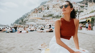 Frau mit rotem Top und weißem Rock und Sonnenbrille am Strand in Positano