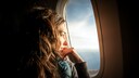 Frau im Flugzeug am Fenster, Sonne scheint ins Gesicht über Meer