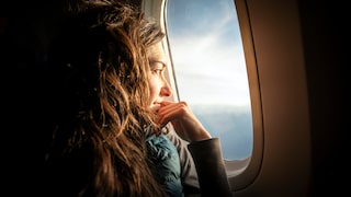 Frau im Flugzeug am Fenster, Sonne scheint ins Gesicht über Meer