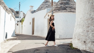 Frau im schwarzen Kleid und weißen Korkpantoletten in einer Gasse in Italien. Könnte vom Look aber auch Griechenland sein. Schön so oder so