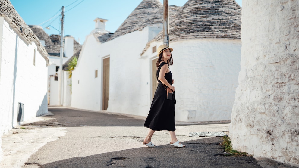 Frau im schwarzen Kleid und weißen Korkpantoletten in einer Gasse in Italien. Könnte vom Look aber auch Griechenland sein. Schön so oder so